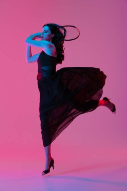 Siyah gece elbisesi giyen, tenis oynayan, pembe neon arka planda soyutlanmış, şık bir kadın. Moda ve spor anlayışı