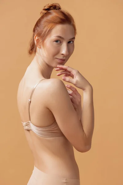 Jonge mooie roodharige vrouw in lingerie poseren geïsoleerd over zand kleur studio achtergrond. Het fitness, dieet, sport, natuurlijke schoonheid en esthetische kosmetologie concept. — Stockfoto
