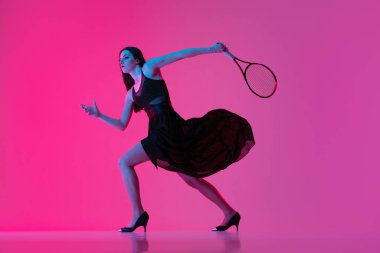Siyah gece elbisesi giyen, tenis oynayan, pembe neon arka planda soyutlanmış, şık bir kadın. Moda ve spor anlayışı