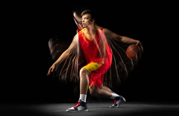 Ein junger Basketballspieler trainiert mit Ball isoliert auf dunklem Hintergrund mit Stroboskopeffekt. Konzept Profisport, Hobby. — Stockfoto