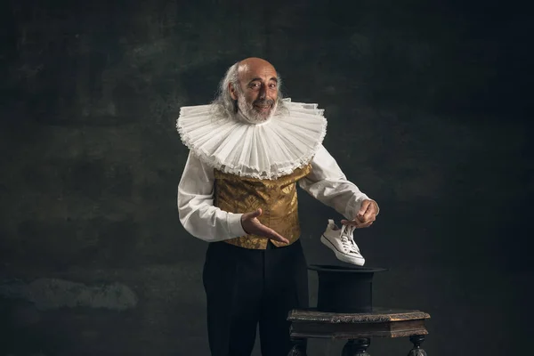 Älterer grauhaariger Mann, Schauspieler oder Zauberer isoliert auf dunklem Vintage-Hintergrund. Retro-Stil, Vergleich des Epochenkonzepts. — Stockfoto
