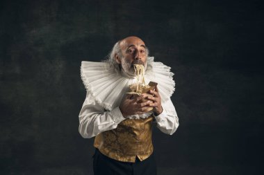 Yaşlı, kır saçlı bir adam, ortaçağ historik kişisi, fast food tatma sanatçısı, koyu renkli arka planda izole edilmiş. Retro biçimi, dönemin karşılaştırması.