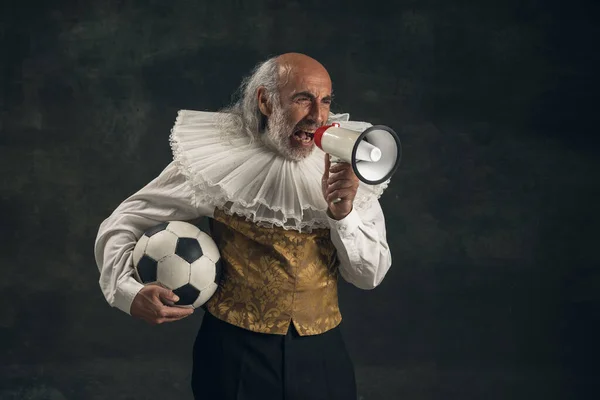 Uomo anziano dai capelli grigi, attore in posa con pallone da calcio isolato su sfondo vintage scuro. Stile retrò, confronto del concetto di epoche. — Foto Stock