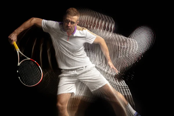 Puissance et vitesse. Jeune homme, joueur de tennis professionnel en mouvement et en action isolé sur fond sombre avec effet stroboscope. — Photo