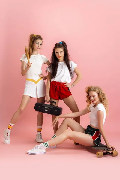 Hübsche junge Frauen im Retro-Stil der 90er Jahre, Outfits, die isoliert vor rosa Studiohintergrund posieren. Konzept des Epochenvergleichs, Schönheit, Mode und Jugend. — Stockfoto