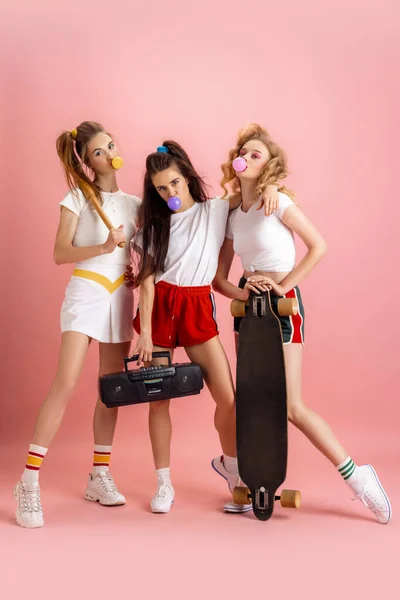 Mulheres muito jovens em retro estilo de moda dos anos 90, roupas posando isolado sobre fundo de estúdio rosa. Conceito de comparação eras, beleza, moda e juventude. — Fotografia de Stock