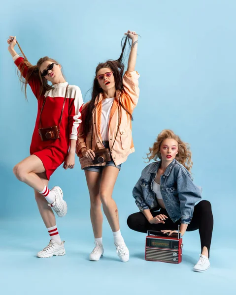 Pretty young women in retro 90s fashion style, outfits posing isolated over blue studio background. Concept of eras comparison, beauty, fashion and youth. — Stock Photo, Image