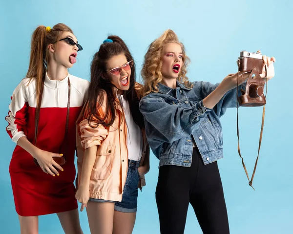 Trois jeunes filles dans le style rétro des années 90, tenues posant isolées sur fond de studio bleu. Concept d'époques comparaison, beauté, mode et jeunesse. — Photo