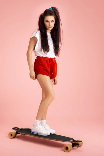 Mooi schattig jong meisje in retro jaren 90 mode stijl, outfits op skateboard geïsoleerd over roze studio achtergrond. Begrip tijdperken vergelijking, schoonheid, mode en jeugd. — Stockfoto