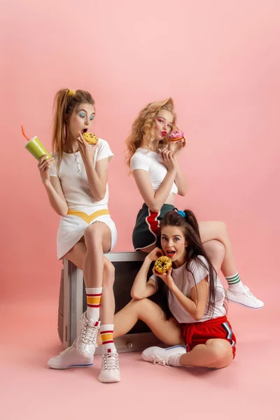 Tres mujeres atractivas jóvenes en estilo de moda retro de los 90, trajes posando aislados sobre fondo de estudio rosa. Concepto de eras comparación, belleza, moda y juventud. — Foto de Stock