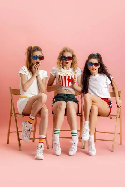 レトロな90年代スタイルの3人の若い女性、ピンクのスタジオの背景に隔離された映画を見ている衣装。時代の概念比較、美しさ、ファッション、若者. — ストック写真