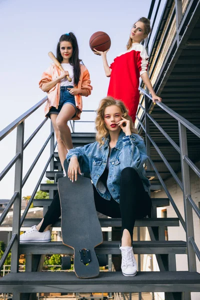 90年代のレトロなファッションスタイルの3人の若い女の子、階段でポーズをとる衣装、屋外。時代の比較、美しさ、ファッション、若者の概念。下の図 — ストック写真