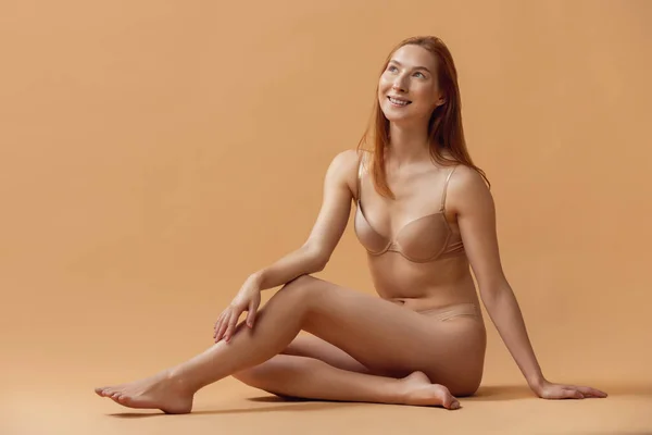 Jeune belle femme rousse en lingerie posant isolée sur fond studio couleur sable. Le concept de fitness, alimentation, sport, beauté naturelle et cosmétologie esthétique. — Photo