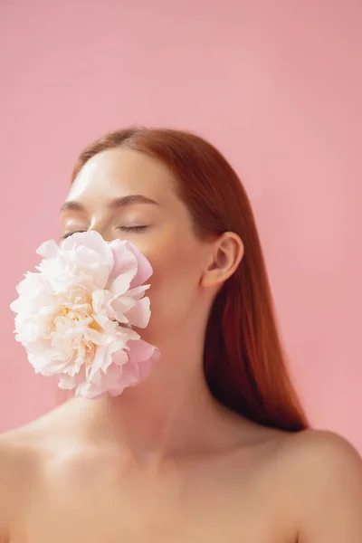 Detailní portrét krásné zrzavé ženy s květinou izolované přes růžové studio zázemí. Nahá barva, strava, kosmetika, přírodní krása a estetická kosmetologie. — Stock fotografie