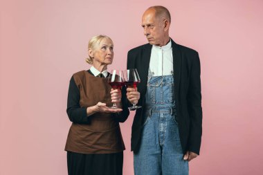 Pembe stüdyo arka planında izole edilmiş eski moda çiftçi kıyafetleri giyen ciddi yaşlı adam ve kadın. Retro tarzı, dönemin ve kültürel konseptin karşılaştırılması.