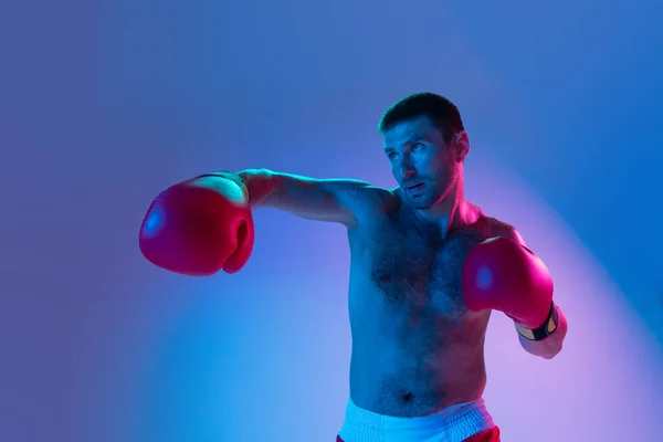 Portrait d'homme caucasien, boxeur professionnel en boxe sportive sur fond studio en dégradé néon. Concept de sport, activité, mouvement, bien-être. — Photo