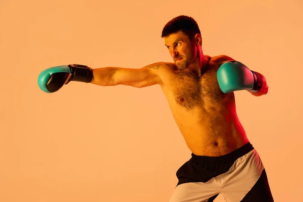 Un boxeador masculino profesional en ropa deportiva y guantes aislados sobre fondo de estudio amarillo en luz de neón. Concepto de deporte, actividad, movimiento, bienestar. — Foto de Stock