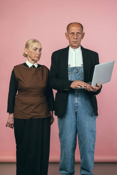 Серйозний літній чоловік і жінка в ретро вінтажних фермерських вбраннях ізольовані на рожевому студійному фоні. Ретро стиль, порівняння епох і культурна концепція . — стокове фото