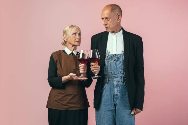 Ernstige oudere man en vrouw in retro vintage boer outfits geïsoleerd op roze studio achtergrond. Retro stijl, vergelijking van tijdperken en cultureel concept. — Stockfoto