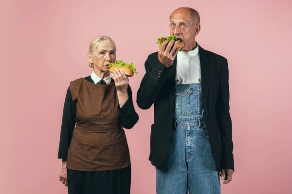 Homem e mulher idosos graves em trajes de agricultor vintage retro isolados em fundo de estúdio rosa. Estilo retrô, comparação de eras e conceito cultural. — Fotografia de Stock