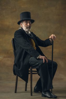 Half-length retro portrait of sad elderly gray-haired man, gentleman, aristocrat or actor isolated on dark vintage background. Retro style, comparison of eras concept.