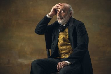Half-length retro portrait of sad elderly gray-haired man, gentleman, aristocrat or actor isolated on dark vintage background. Retro style, comparison of eras concept.