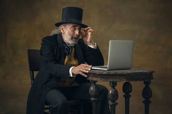 Half-length retro portrait of sad elderly gray-haired man, gentleman, aristocrat or actor isolated on dark vintage background. Retro style, comparison of eras concept. — Stockfoto