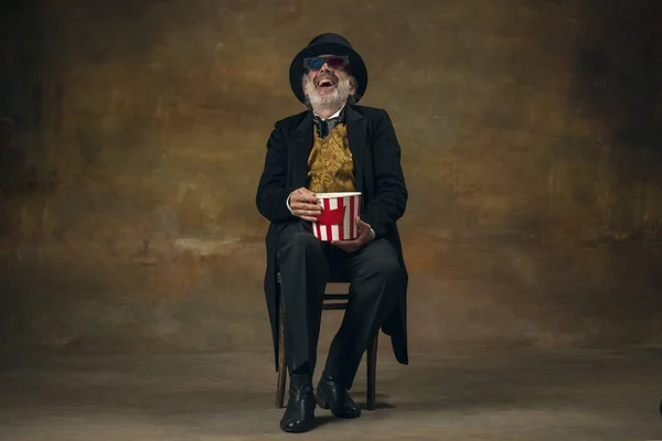 Bonito homem sorridente sênior, cavalheiro, aristocrata ou ator assistindo filme isolado em fundo escuro vintage. Estilo retro, comparação do conceito eras. — Fotografia de Stock