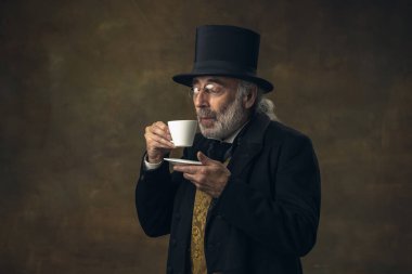 Portrait of elderly gray-haired man, gentleman, aristocrat or actor isolated on dark vintage background. Retro style, comparison of eras concept.