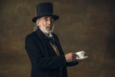 Portrait of elderly gray-haired man, gentleman, aristocrat or actor isolated on dark vintage background. Retro style, comparison of eras concept.