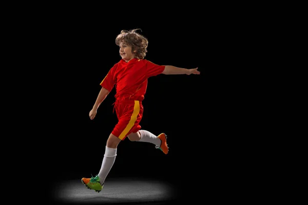 Um pequeno jogador de futebol masculino, treinamento de meninos com bola de futebol isolada no fundo do estúdio escuro. Conceito de esporte, jogo, hobby — Fotografia de Stock