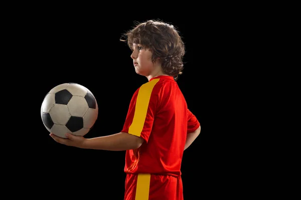 Retrato de menino, jogador de futebol posando com bola de futebol isolado no fundo escuro estúdio. Conceito de esporte, jogo, hobby e infância — Fotografia de Stock