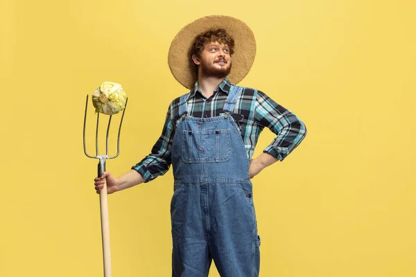 Portrait of young man, farmer with garden equipment isolated over yellow studio background. Concept of professional occupation, work. — Foto de Stock