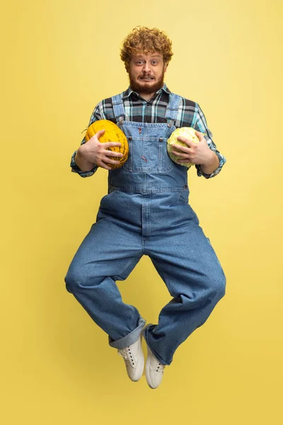 Portré göndör szakállú férfiról, gazdáról, nagy dinnyével a sárga stúdió hátterében. A szakmai foglalkozás fogalma, munka. — Stock Fotó