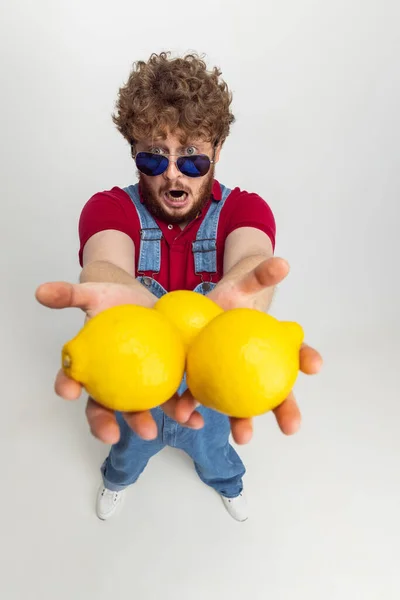 Vue en angle élevé de drôle de jeune homme, agriculteur avec de gros citrons debout isolé sur fond de studio gris. Notion de profession, de travail. — Photo