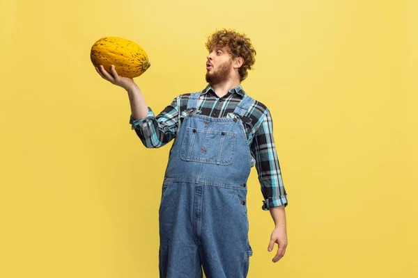 Portrait of curly bearded man, farmer with big melon standing isolated over green studio background. Concept of professional occupation, work. — Foto de Stock