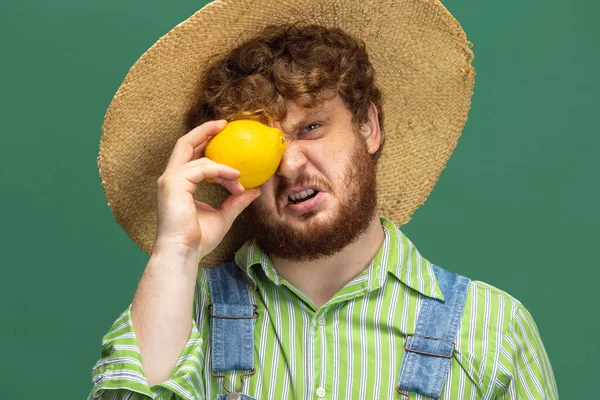 Close-up funny redheaded bearded man, farmer with yellow pepper standing isolated over green studio background. Concept of professional occupation, work. — Foto Stock