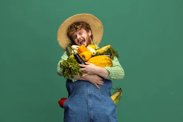 Рыжеволосый бородатый человек, фермер с овощами, стоящий в изоляции на зеленом фоне студии. Концепция профессиональной профессии, работы. — стоковое фото