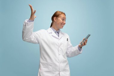 Kadın doktor portresi, tedavi edici ya da tıbbi danışman mavi arka planda izole edilmiş akıllı telefon ekranlı. Komik mutlu duygular. Sağlık, bakım, tıp ve mizah kavramı