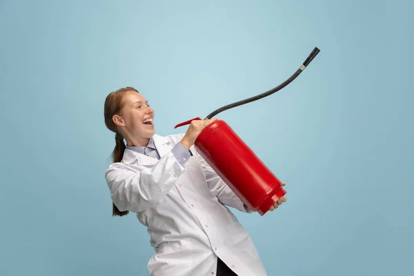 Portret van jonge vrouw, dokter, therapeutisch of medisch adviseur met brandblusser geïsoleerd op blauwe achtergrond. Grappige meme emoties. — Stockfoto