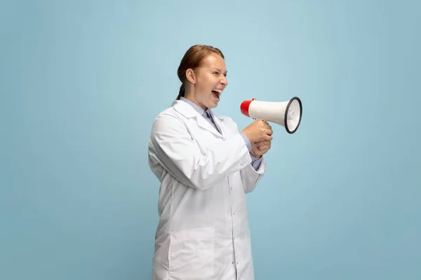 Een vrouwelijke arts, therapeutisch of medisch adviseur schreeuwend naar megafoon geïsoleerd op blauwe achtergrond. Concept van emoties, gezichtsuitdrukkingen, gezondheidszorg en geneeskunde — Stockfoto