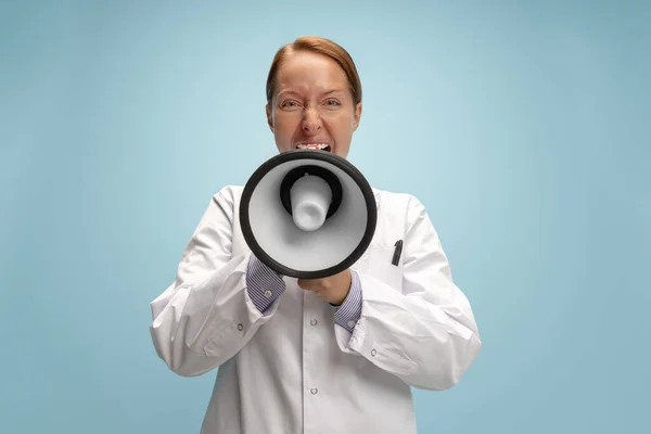En kvinnlig läkare, terapeutisk eller medicinsk rådgivare ropar på megafon isolerad på blå bakgrund. Begreppet känslor, ansiktsuttryck, hälsovård och medicin — Stockfoto