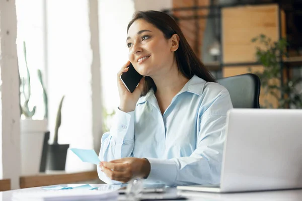 Young Caucasian woman, business lady during working office day. Using laptop, modern gadgets. Remote working. Workplace at office with PC, devices. — Foto de Stock