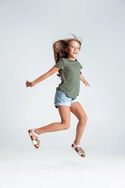 Retrato de comprimento total de belo pré-escolar sorrindo menina pulando, jogando isolado no fundo do estúdio cinza. Copyspace para anúncio. Infância, educação, conceito de emoção — Fotografia de Stock