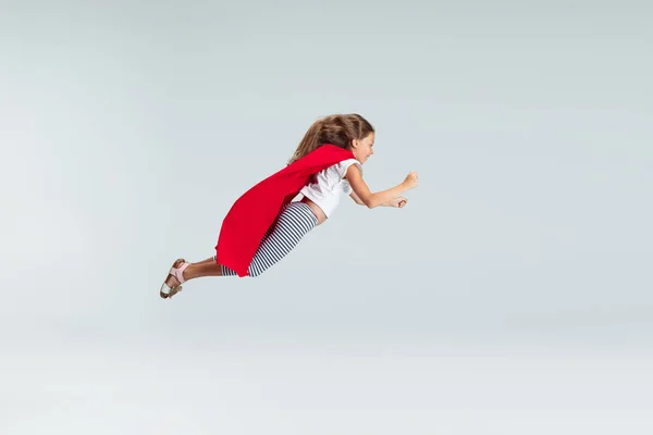 Pełnowymiarowy portret pięknej dziewczynki latającej jak superbohater w czerwonej pelerynie odizolowanej na szarym tle studia. Dzieciństwo, edukacja, koncepcja emocji. Ulotka — Zdjęcie stockowe