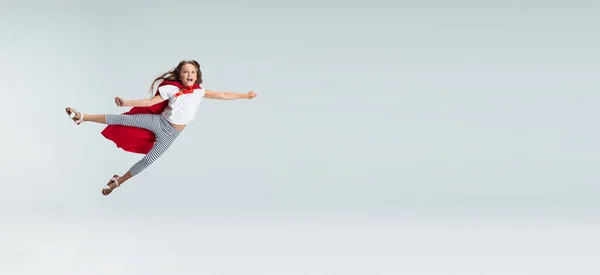 Полнометражный портрет красивой маленькой девочки, летящей как супергерой в красной накидке, изолированной на сером фоне студии. Детство, образование, эмоциональная концепция. Flyer — стоковое фото