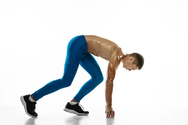 Vista lateral. Retrato de un joven atleta profesional, corredor aislado sobre fondo blanco del estudio. Hombre musculoso y deportivo. Concepto de deporte, estilo de vida saludable —  Fotos de Stock