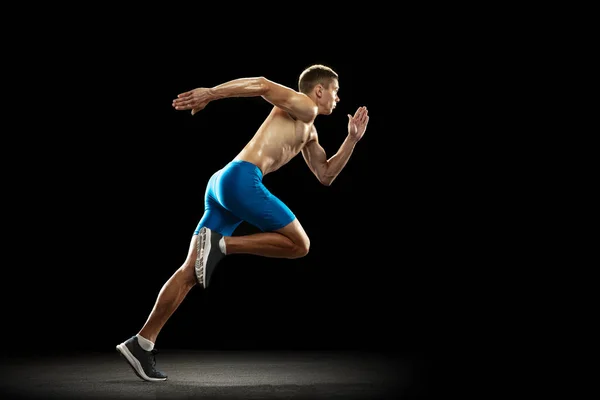 Un atleta masculino profesional caucásico, entrenamiento de corredor aislado en el fondo oscuro del estudio. Hombre musculoso y deportivo. Concepto de deporte, estilo de vida saludable — Foto de Stock