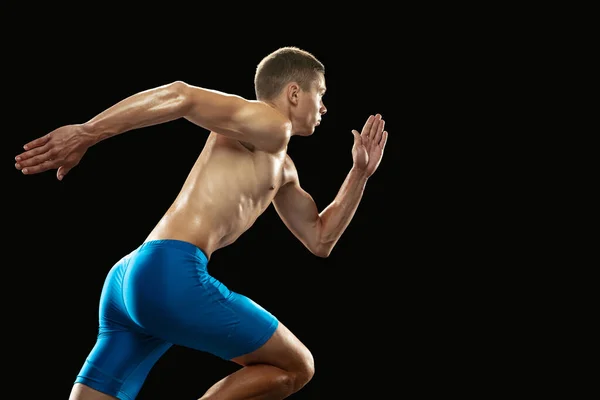 Joven atleta profesional masculino, entrenamiento de corredor aislado en el fondo oscuro del estudio. Hombre musculoso y deportivo. Concepto de deporte, estilo de vida saludable — Foto de Stock