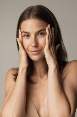 Gri stüdyo arkaplanından izole edilmiş makyajsız genç ve zayıf bir kadının yakın plan portresi. Doğal güzellik konsepti.